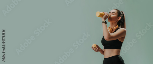 Foto Young sporty woman in sportswear with wireless headset drinking from bottle over