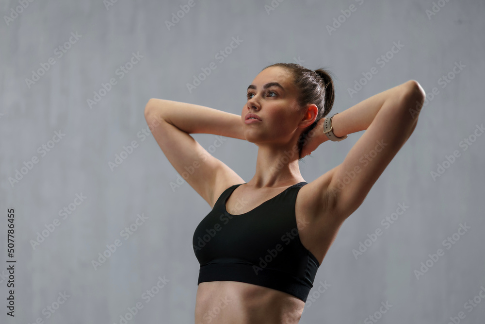 Fototapeta premium Young sporty woman in sports clotheswith arms behind head against beige background, copy space