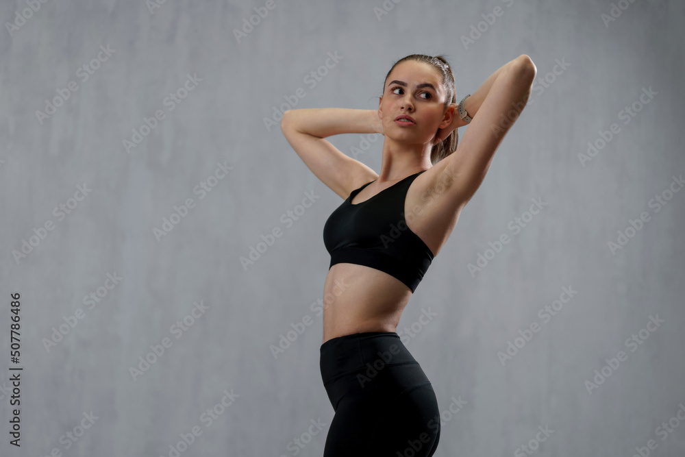 Obraz premium Sports woman in fashion black sport clothes posing in gym, over gray background