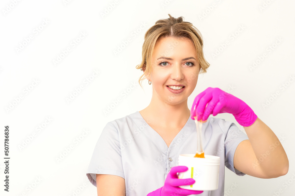 Portrait of a female caucasian beautician holding a jar of sugar paste for sugaring wearing pink gloves on white background Portrait of a female caucasian beautician holding a jar of sugar paste for sugaring wearing pink gloves on white background