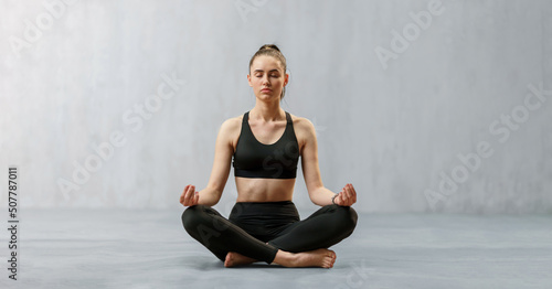 Fotografie, Obraz Young healthy woman in black sportsclothes practising yoga in studio, in a yoga