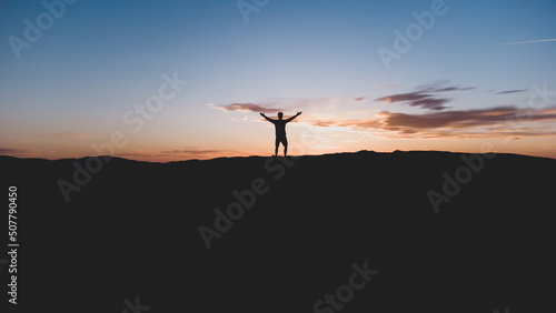 Silueta de persona, con los brazos levantados en el desierto en la hora del amanecer. Fotografía horizontal con espacio para texto.