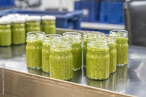 Pesto sauce Industrial process. High quality sauce production. Green pesto sauce in open jars on a food factory table. Italian basil taste in Pesto sauce