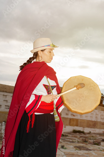 South American native woman with typical costume playing a small drum in a colonial construction