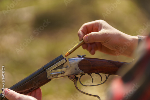 Close-up of hunter man charges the cartridge on rifle gun in forest. photo