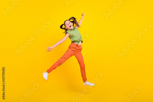 Photo of carefree pretty student girl wear green shirt smiling jumping high arm sides isolated yellow color background