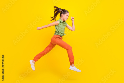 Photo of funky pretty student girl wear green shirt smiling running fast jumping high isolated yellow color background