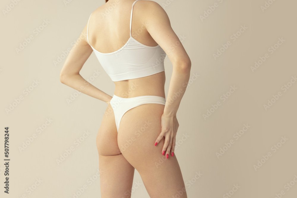 Cropped back view image of slim female body, buttocks in white cotton underwear isolated over grey studio background. Anti-cellulite treatment