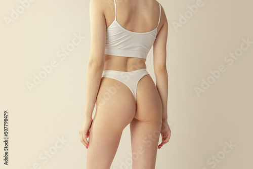 Cropped image of slender female body, back and buttucks in white cotton underwear isolated over grey studio background