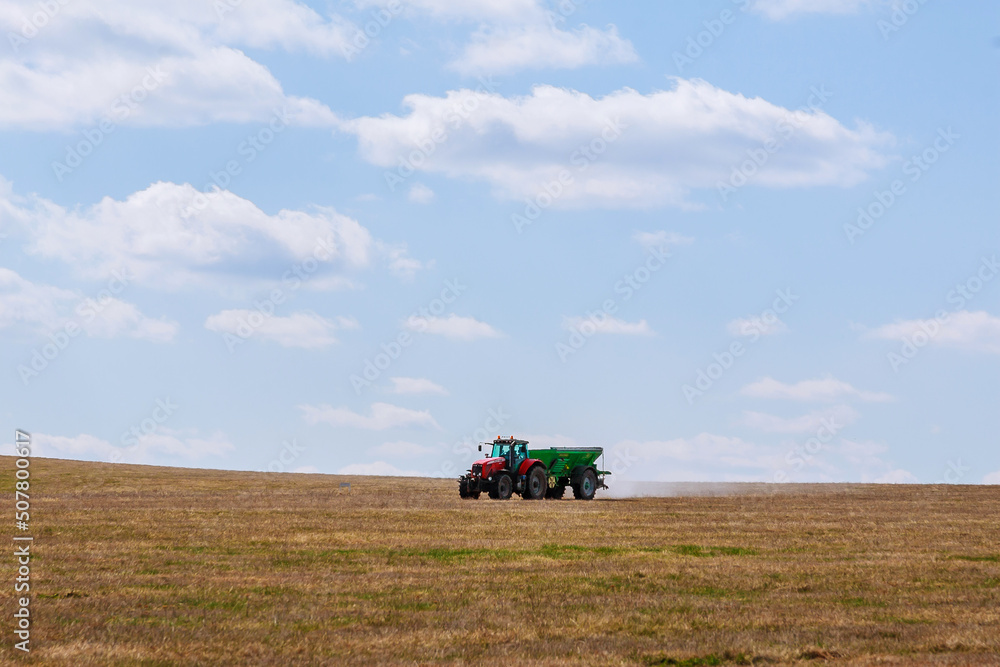 Fototapeta premium A red tractor in a green trailer is carrying fertilizer. Agricultural work is performed by a farmer.