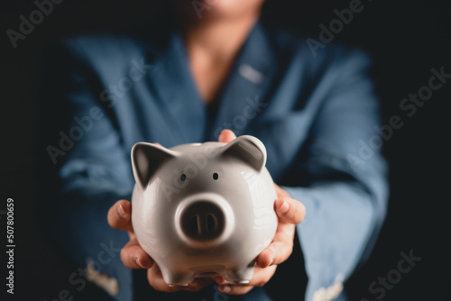 a business woman wearing a suit holding a piggy bank of a white pig money saving concept 