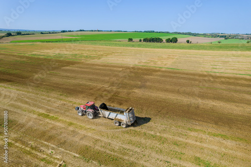 Top view of a tractor moving across a field with an empty trailer.