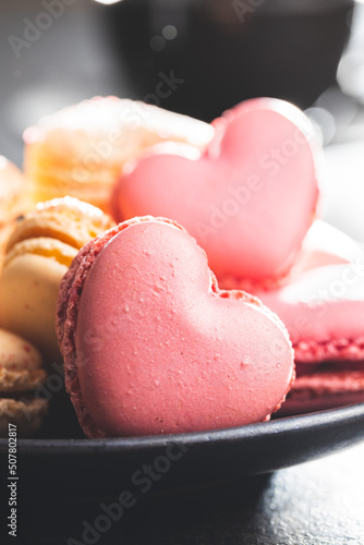 Heart shaped Sweet macarons on plate on black table.