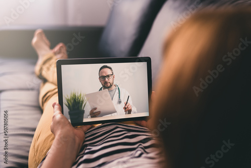 Woman lying on a sofa and talking with a doctor online using digital tablet. Telemedicine concept. photo