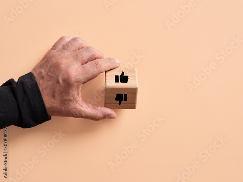 Hand turns the wooden cube with like and dislike, thumb up and down symbols.