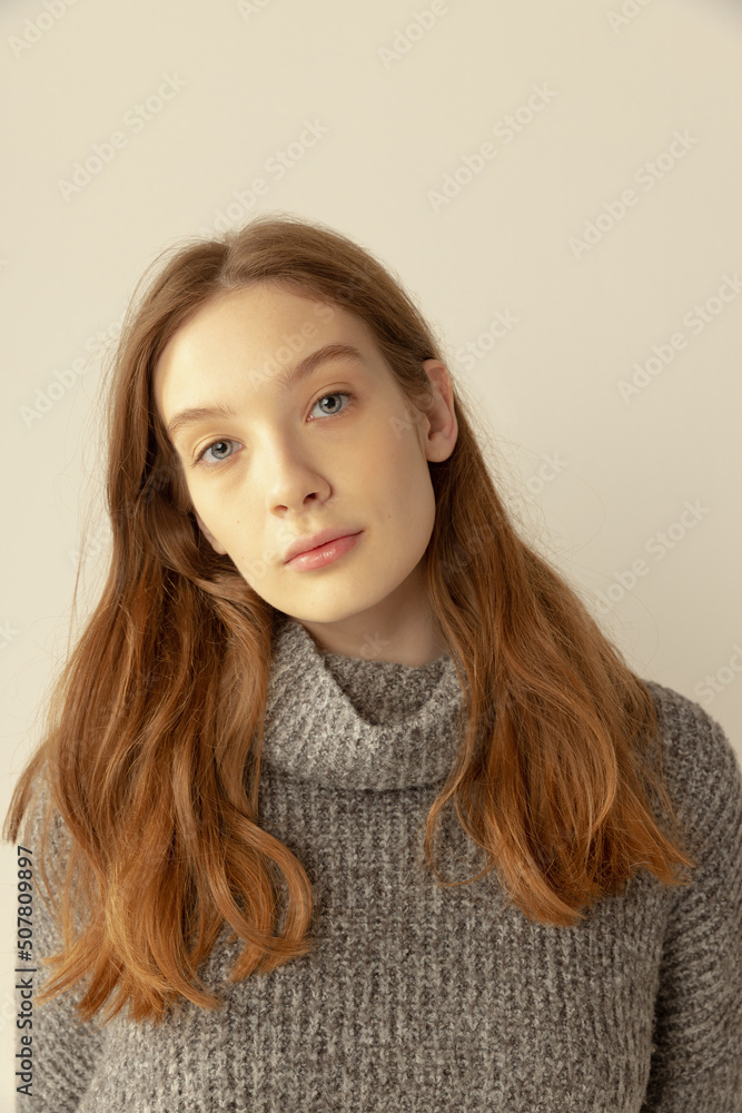 Portrait of young red-haired girl in sweater posing, looking at camera isolated over grey studio background. Portrait of young red-haired girl in sweater posing, looking at camera isolated over grey studio background.