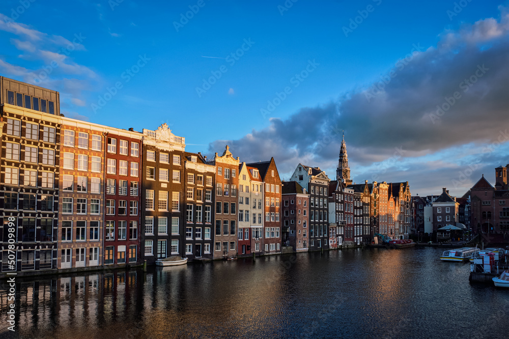 Houses and tourist boats on Amsterdam canal pier Damrak on sunset. Amsterdam, Netherlands