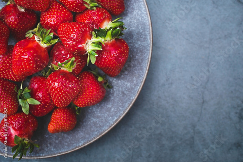 Delicious, fresh strawberries in a stylish plate on a concrete background. Top view with space to copy.