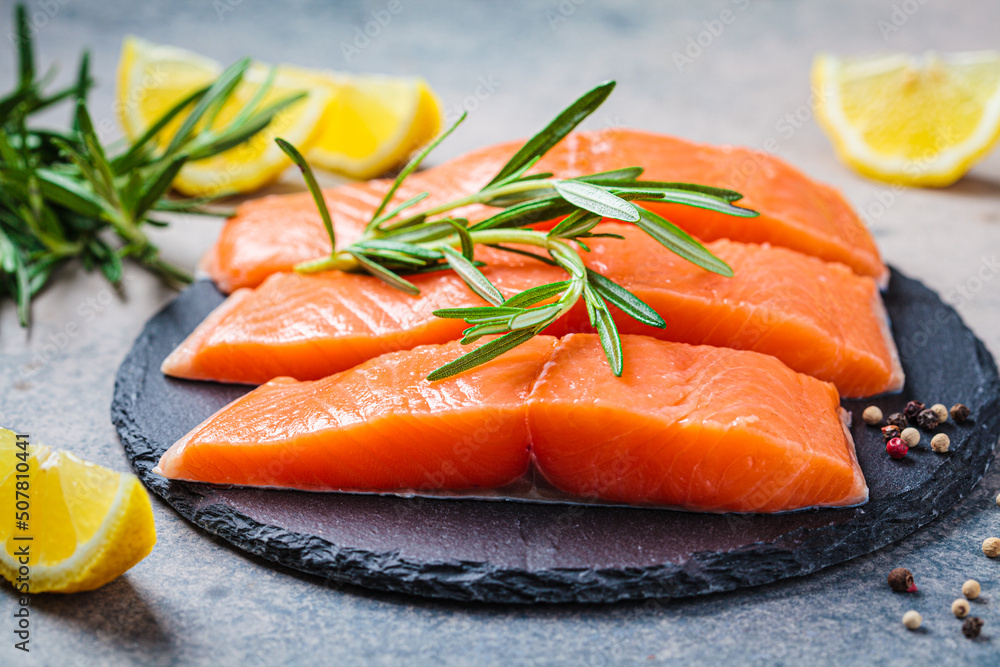 Pieces of raw salmon with spices and herbs on slate board, dark background. Pieces of raw salmon with spices and herbs on slate board, dark background.
