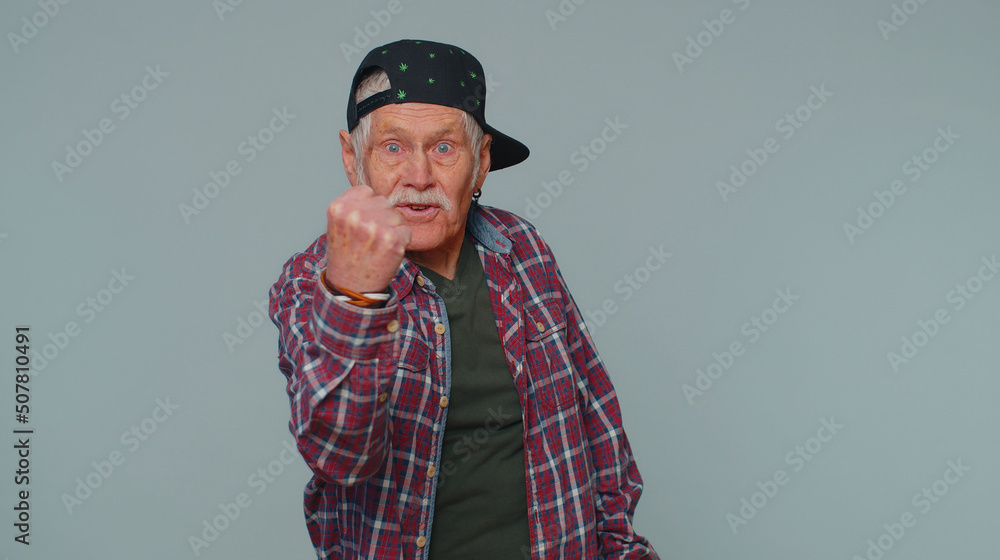 Aggressive angry senior man 80s in shirt trying to fight at camera, shaking fist, boxing with expression, punishment, disappointment. Elderly grandfather isolated alone on gray studio wall background Aggressive angry senior man 80s in shirt trying to fight at camera, shaking fist, boxing with expression, punishment, disappointment. Elderly grandfather isolated alone on gray studio wall background