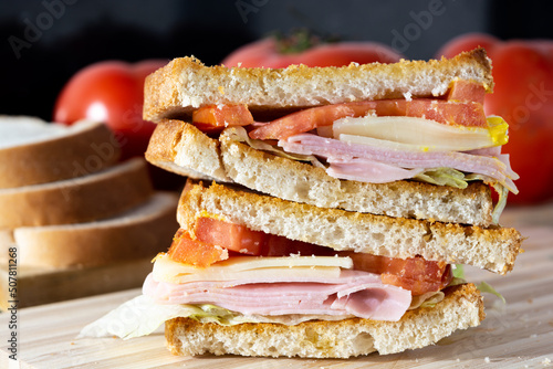 sandwich made of toast, tomato, cheese, ham, lettuce and mustard on wooden surface