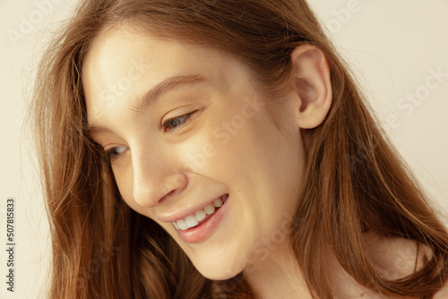 Close-up portrait of beautiful young red-haired girl posing, tenderly smiling isolated over grey studio background
