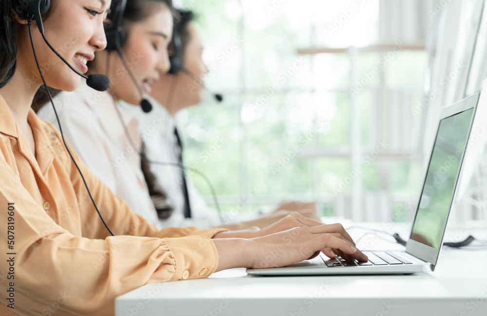 Selective focus on hand of young operator woman typing and working with headset smiling and doing customer support at work. Group of Asian employee work in telemarketing customer service teams Selective focus on hand of young operator woman typing and working with headset smiling and doing customer support at work. Group of Asian employee work in telemarketing customer service teams