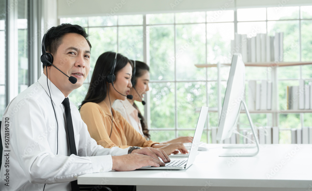 Group of Asian employee work in telemarketing customer service teams. Young operator man working with headset smiling and doing customer support at work. Call Center with service mind concept Group of Asian employee work in telemarketing customer service teams. Young operator man working with headset smiling and doing customer support at work. Call Center with service mind concept
