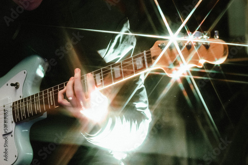 Young man playing on electric guitar on dark background with light effect