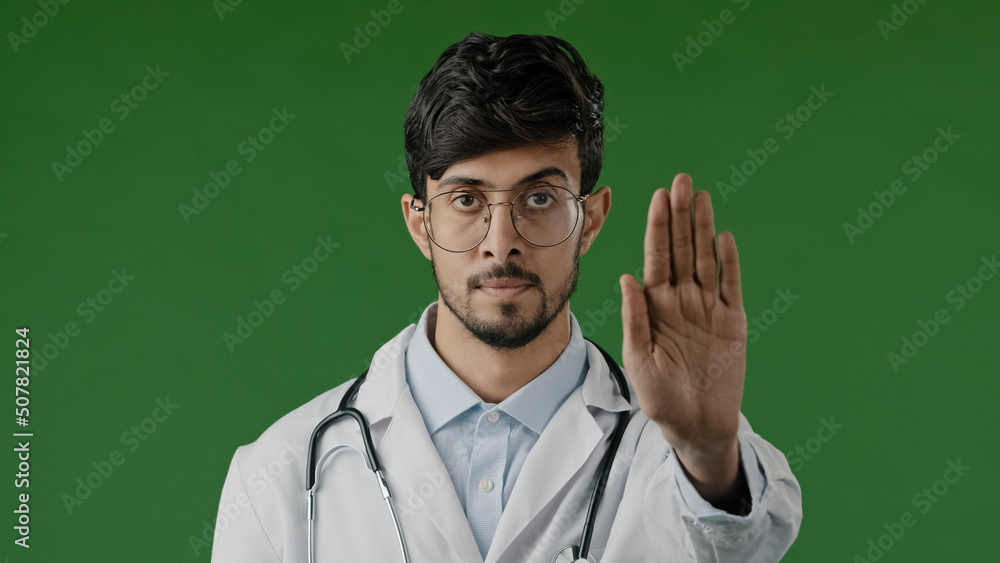 Young male doctor man in medical mask isolated in green chroma key studio show stop sign with prohibitive hand gesture safe distance puts palm forward disagreeing stop coronavirus infection spreading Young male doctor man in medical mask isolated in green chroma key studio show stop sign with prohibitive hand gesture safe distance puts palm forward disagreeing stop coronavirus infection spreading