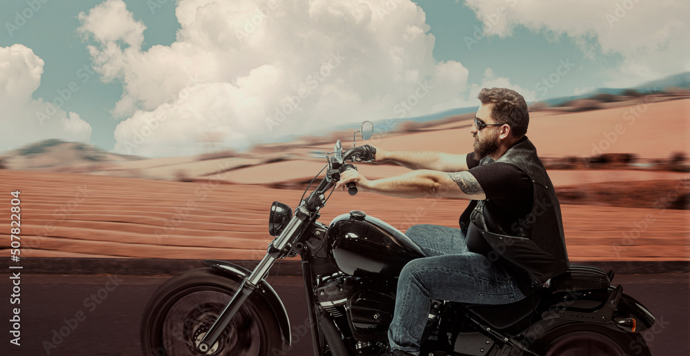 Fototapeta premium Stylish brutal biker riding motorbike in speed highway in summer evening time. Vintage cinematic background and dramatic cloudy sky. Concept of fashion, style and hobby