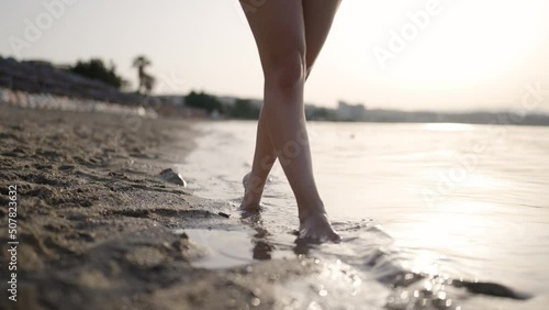 Slow motion sexy woman feet walking barefoot with tanga string bikini by beach at golden sunset leaving footprints in sand. Female tourist on summer vacation.