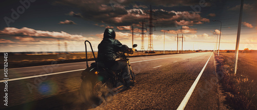 Fotografija Stylish brutal biker riding motorbike in speed highway in summer evening time