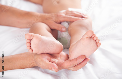 Grandmother showing legs of little baby on bed. © andranik123