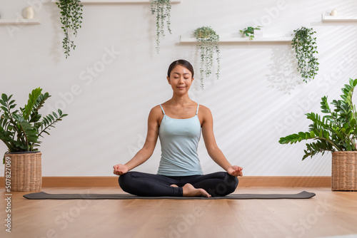 Calm of wellness Asian young woman sit on yoga mat doing breathing with yoga lotus pose.Yoga meditation of young healthy woman relax and comfortable at white cozy home,Yoga Exercise Wellness Concept