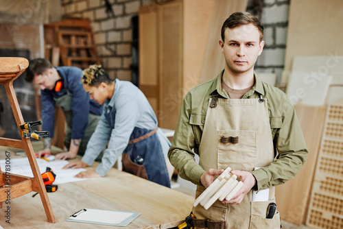 Waist up portrait of young carpenter in coveralls looking at camera while posing in artisan workshop, copy space