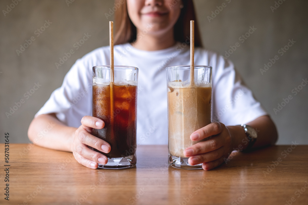 Closeup image of a young woman holding and drinking two glasses of iced coffee Closeup image of a young woman holding and drinking two glasses of iced coffee