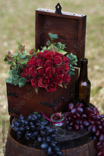 Bouquet of red roses in a wooden box. Nearby is a bottle of wine and grapes. For a catalog or online store. Floral shop concept. Beautiful freshly cut bouquet. flower delivery