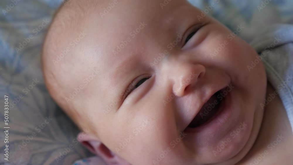 Adorable little girl with plump cheeks smiles wide lying on soft bed at home. Portrait of sweet newborn baby in bodysuit feeling happily closeup Adorable little girl with plump cheeks smiles wide lying on soft bed at home. Portrait of sweet newborn baby in bodysuit feeling happily closeup