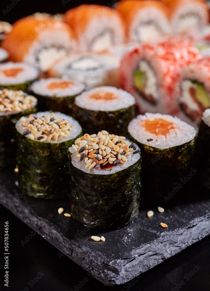 Close up of rolls with sauce and sesame seeds on a black flat plate. Close up of rolls with sauce and sesame seeds on a black flat plate.