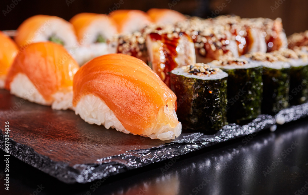 Traditional sashimi sushi with salmon on a black flat board.
