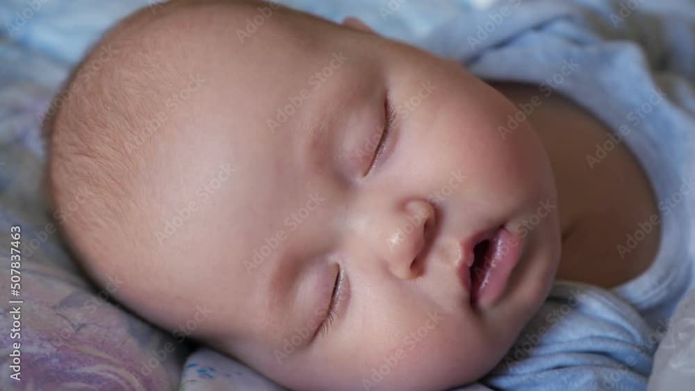 Adorable newborn girl with closed eyes sleeps peacefully in bed. Portrait of little baby with plump cheeks at daytime sleep in nursery extreme closeup Adorable newborn girl with closed eyes sleeps peacefully in bed. Portrait of little baby with plump cheeks at daytime sleep in nursery extreme closeup