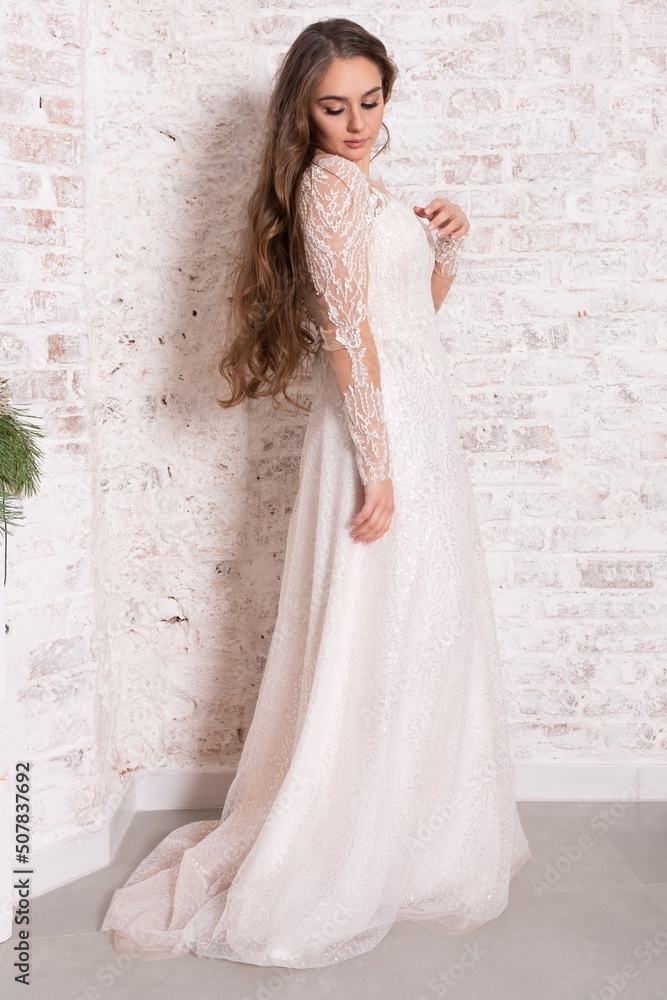 Fototapeta premium Bride in a white dress against a brick wall.