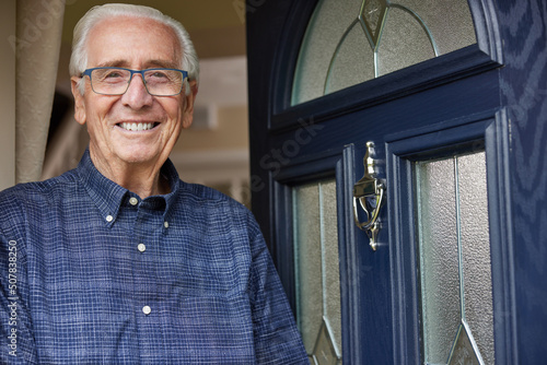 Portrait Of Smiling Senior Man Standing At Open Front Door Of House photo