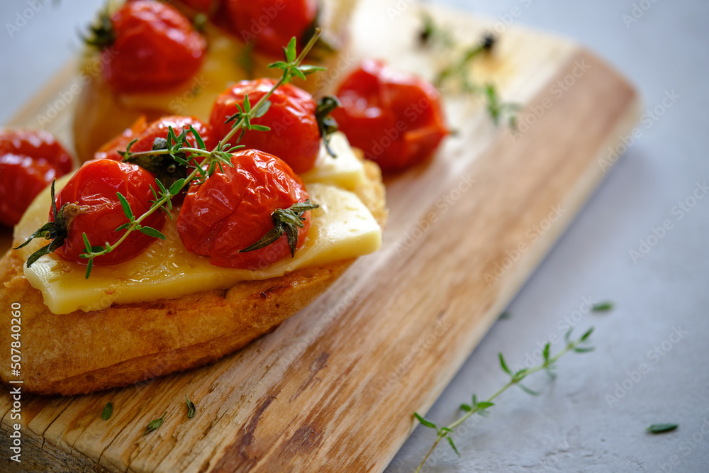 Fried slices of fresh bread with cheese and cherry tomatoes on a wooden board on a gray background. T Fried slices of fresh bread with cheese and cherry tomatoes on a wooden board on a gray background. T