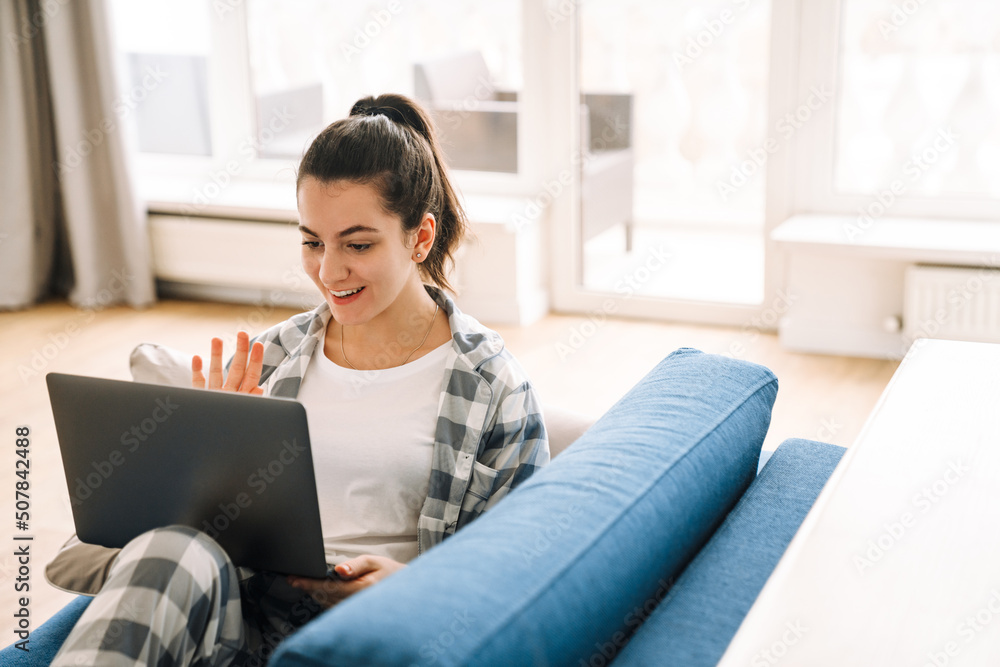 Young woman gesturing and using laptop while resting on couch Young woman gesturing and using laptop while resting on couch