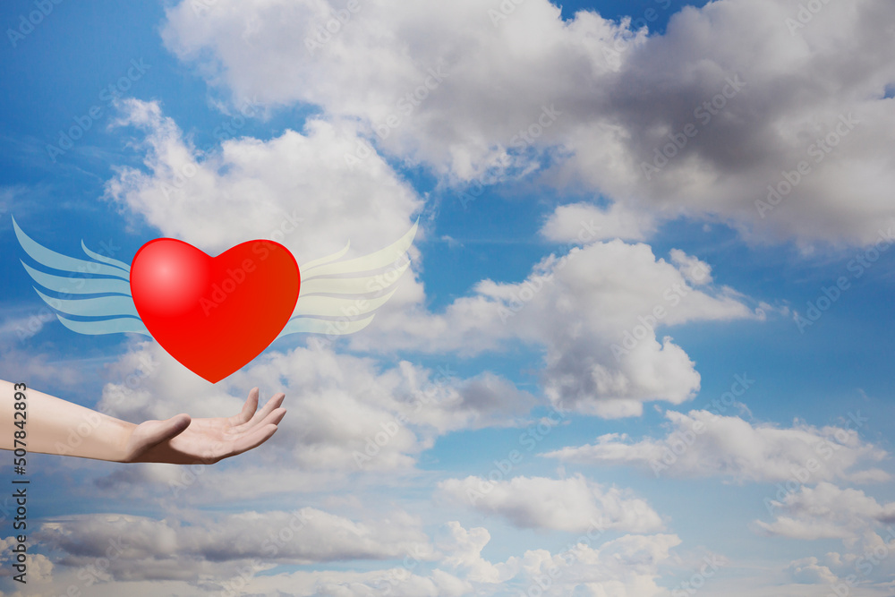 Hand holding heart shape with wings on blue sky. Valentine decorative symbol concept. 3D rendering image.