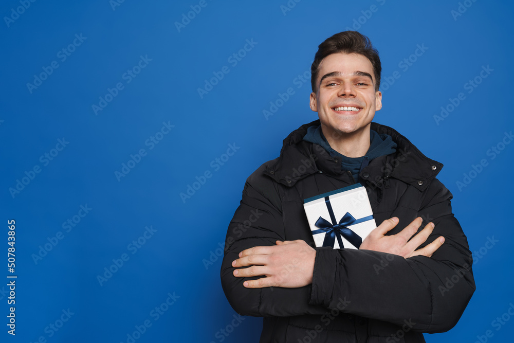 Young white man smiling while posing with gift box Young white man smiling while posing with gift box
