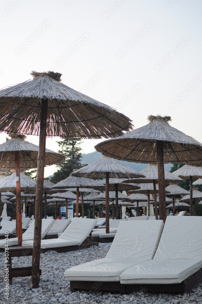 Sunbeds with straw umbrellas on the pebble beach. No people in evening time