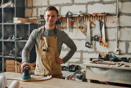 Fotografija Warm toned shot of young carpenter smiling at camera while building furniture in